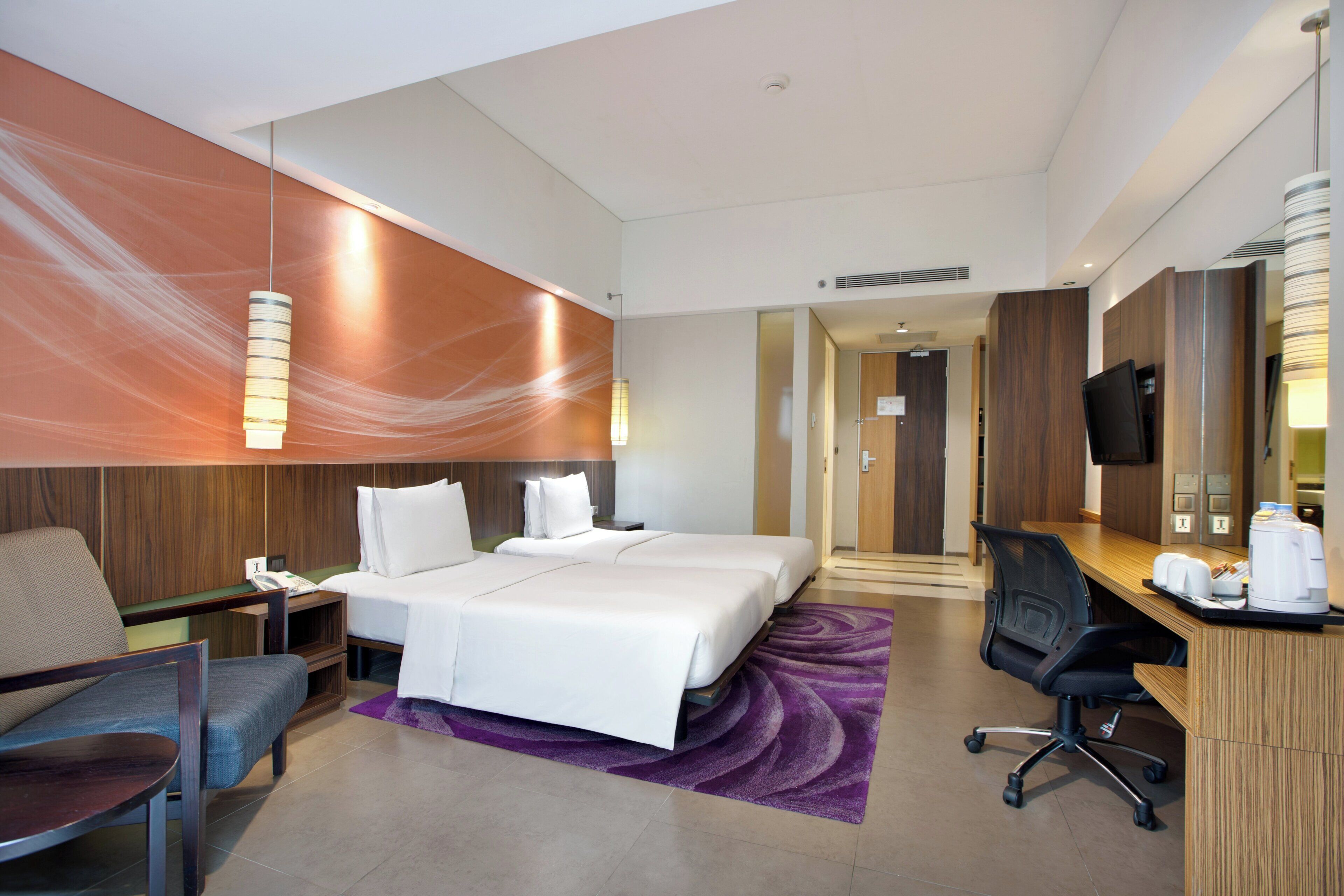 Une chambre d’hôtel avec deux lits, un bureau, une chaise, une lampe de bureau et un téléviseur.