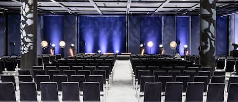 An auditorium with rows of chairs, a stage with lighting, and a blue wall with a pattern.