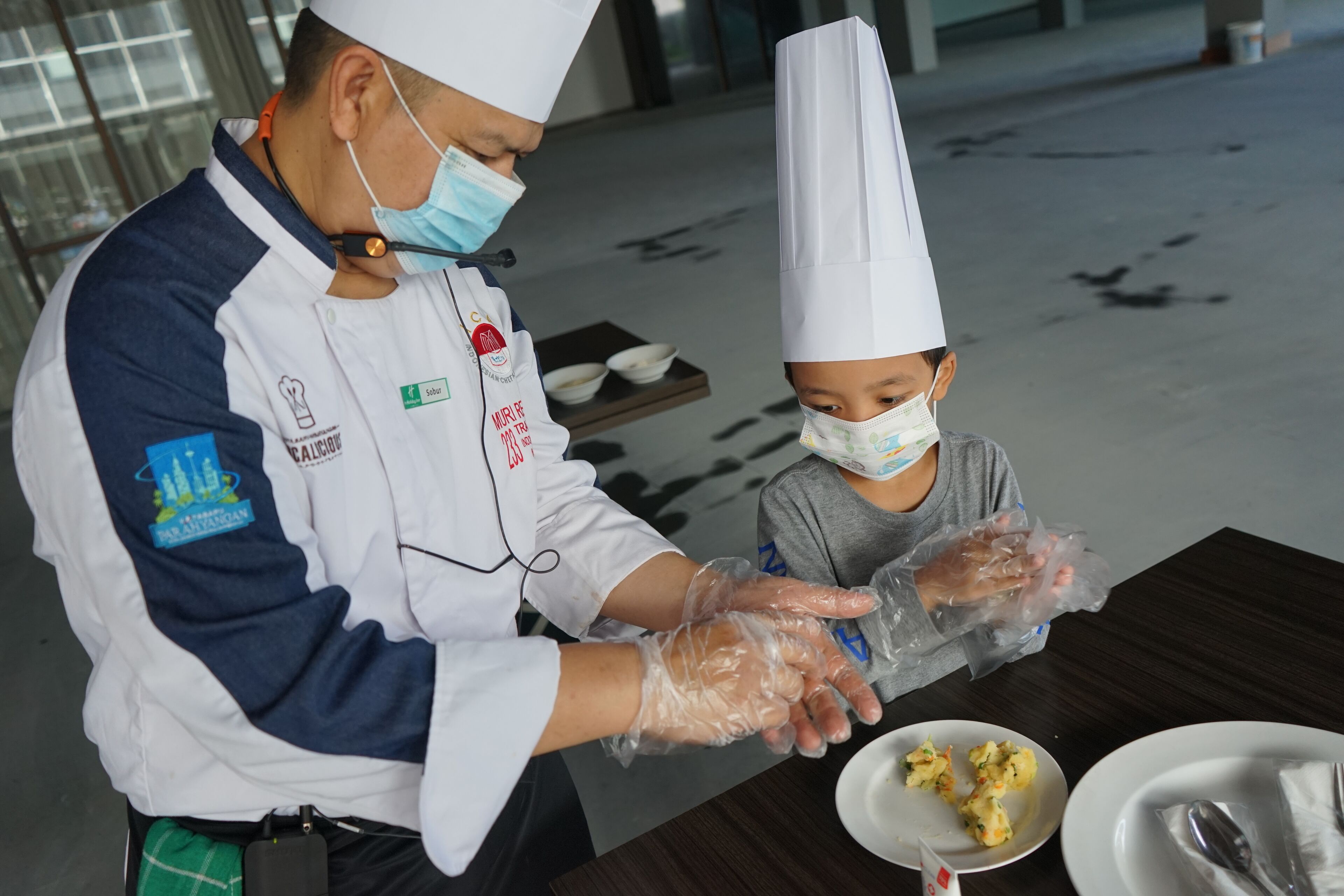 A person in a chef's uniform serving food to a child at a table.