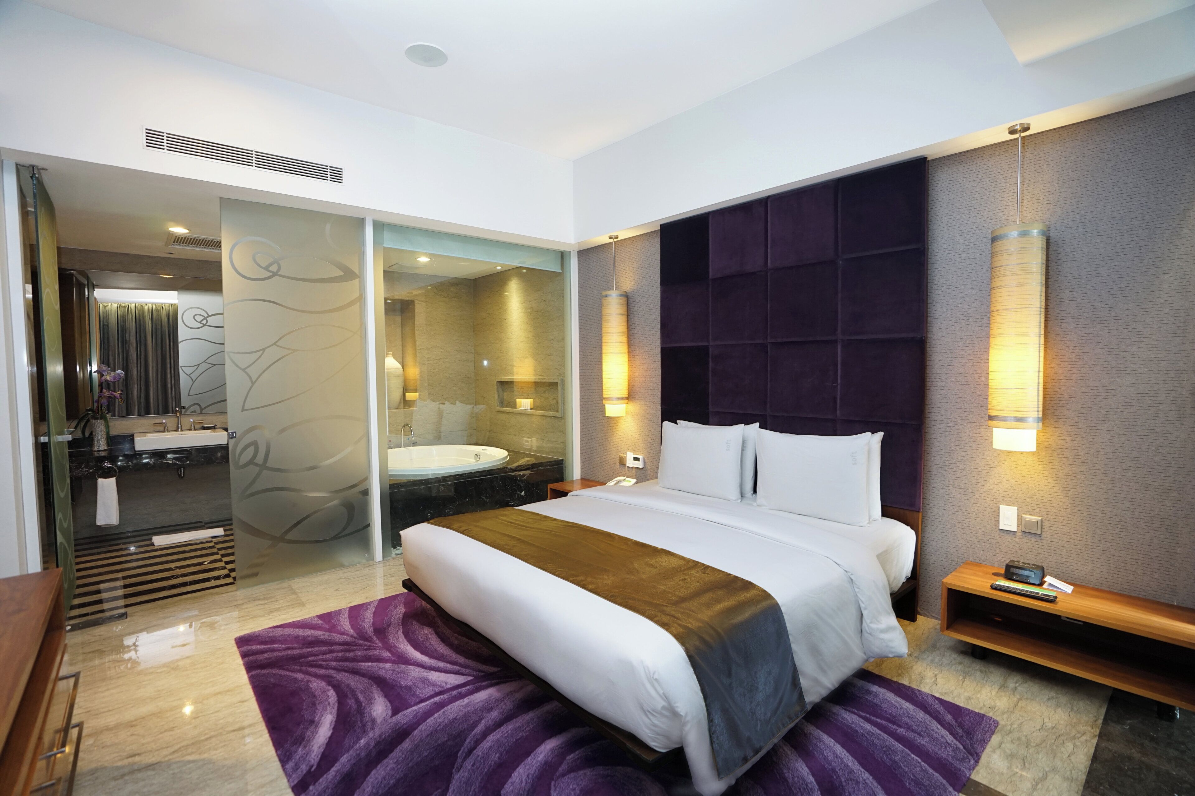 Una habitación de hotel moderna con una cama grande, un baño con bañera y un separador de vidrio.