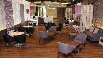 A modern lounge area with round tables, sofas, and chairs arranged on a wooden floor.