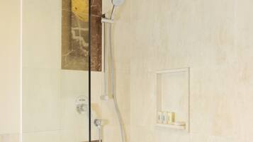 A modern shower area with a glass partition, a handheld showerhead, and a wall-mounted control panel.