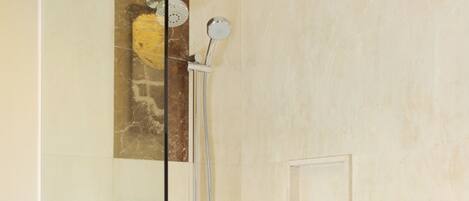 Un área de ducha moderna con separador de vidrio, cabezal de ducha de mano y panel de control en la pared.