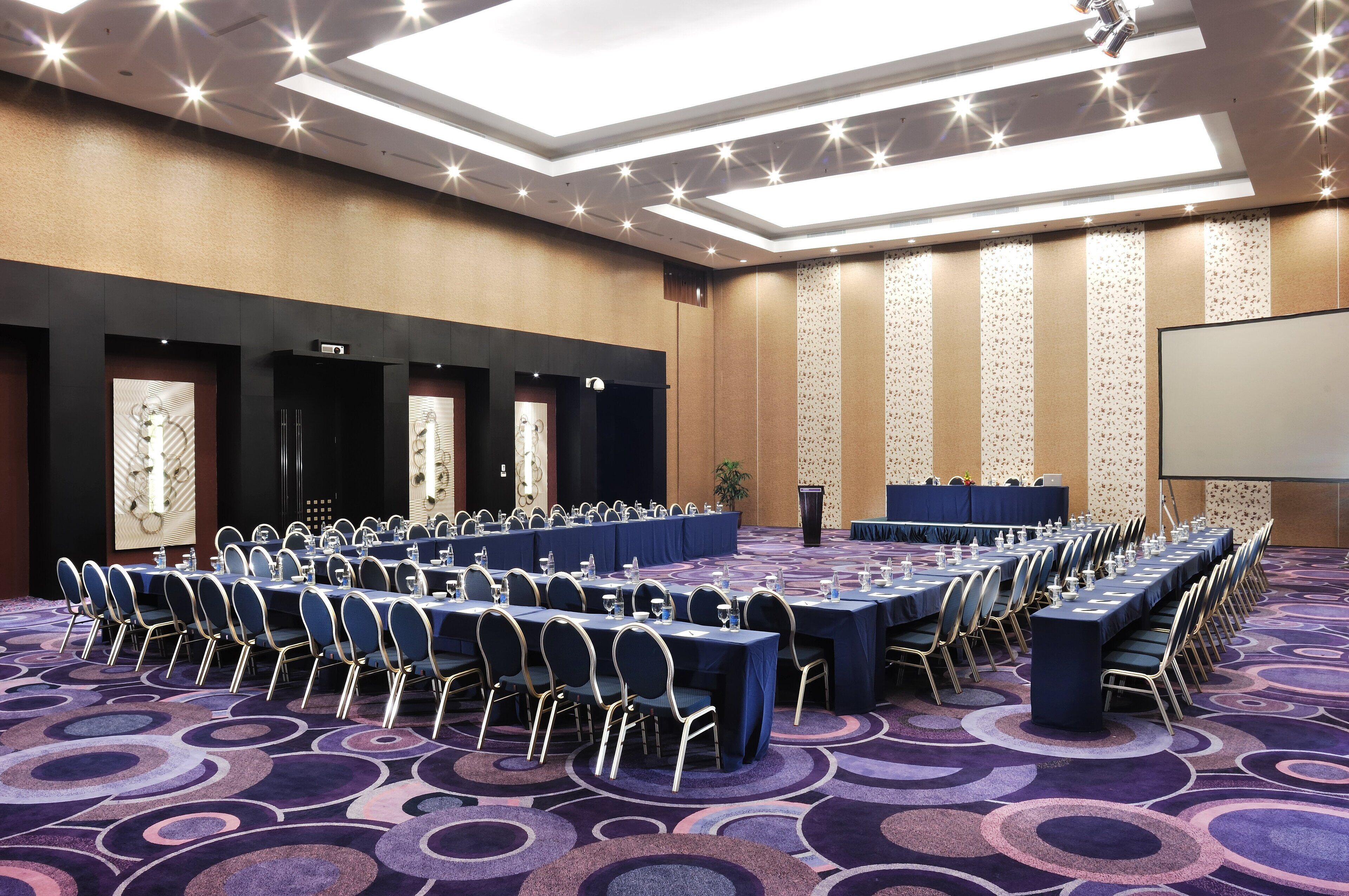 A conference room with long tables, chairs, and a projector screen.