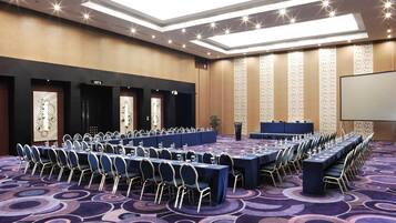 A conference room with long tables, chairs, and a projector screen.