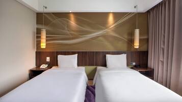 Una habitación de hotel con dos camas, un cabecero de madera, una lámpara fijada a la pared y un teléfono en la mesita de noche.
