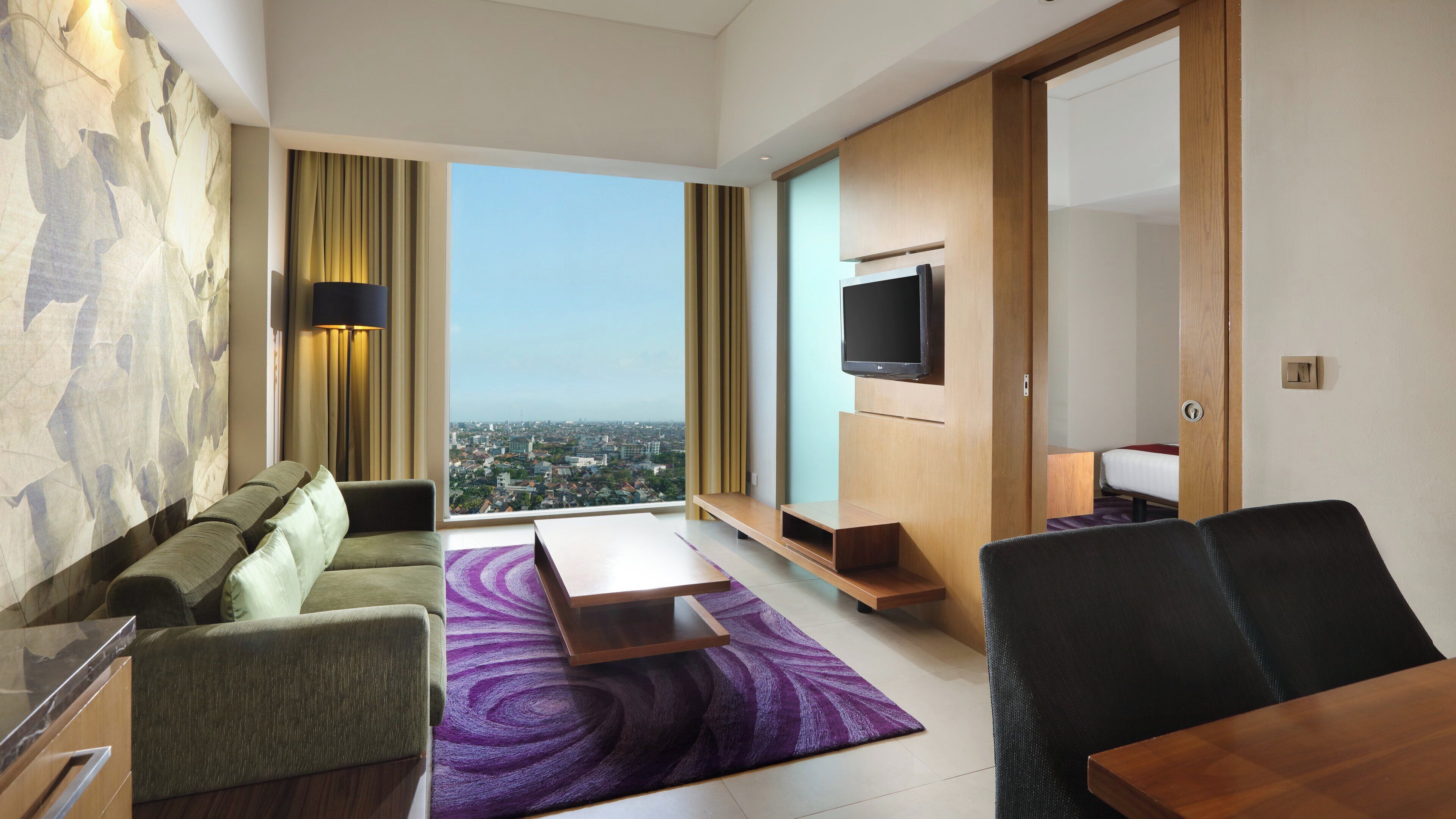 Ein modernes Hotelzimmer mit Blick auf die Stadt, einer Couch, einem Couchtisch, einem Fernseher und einem Holzkasten.