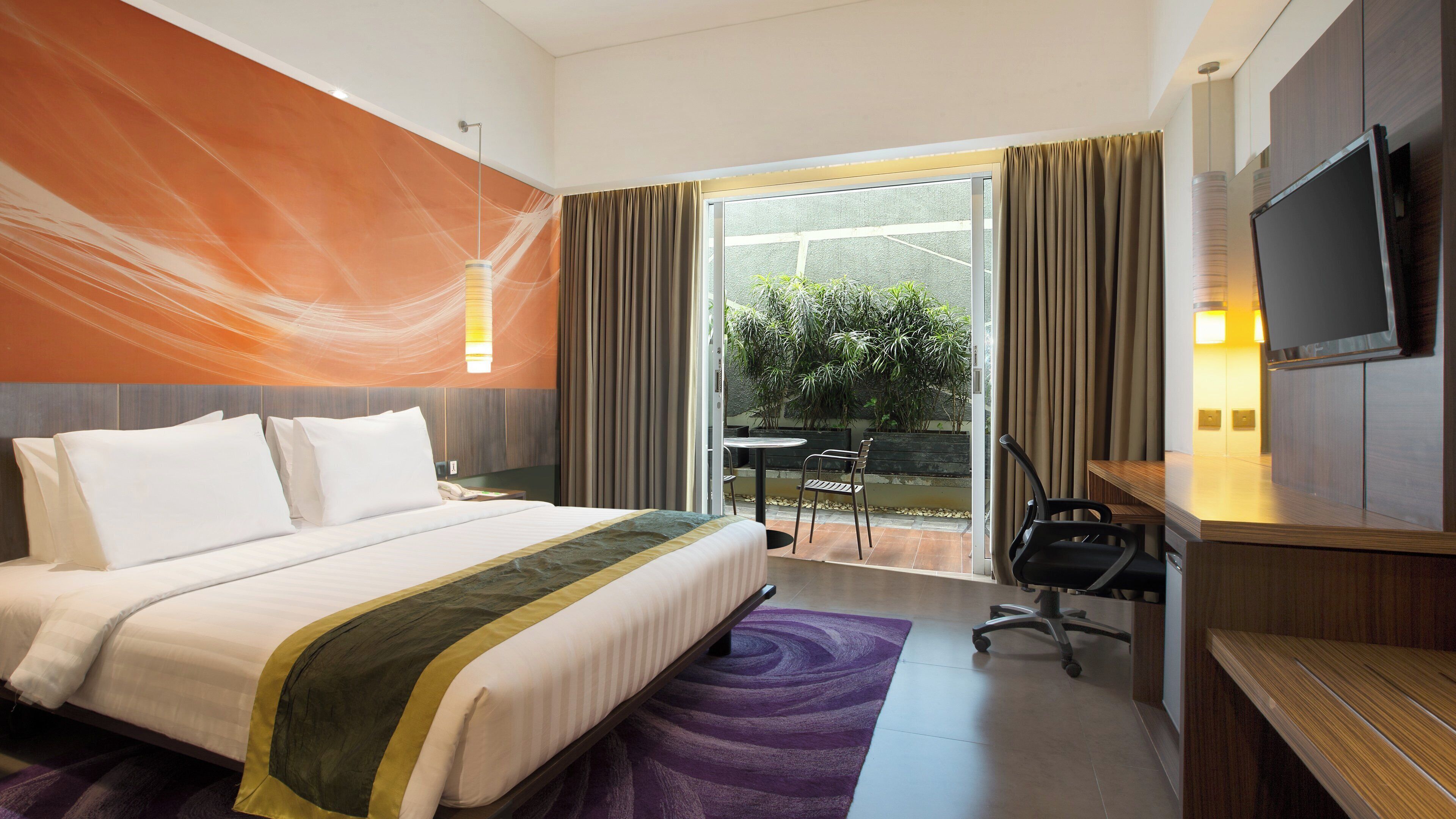 Habitación de hotel con una cama grande, un escritorio con silla, televisión y vistas a un jardín a través de la ventana.