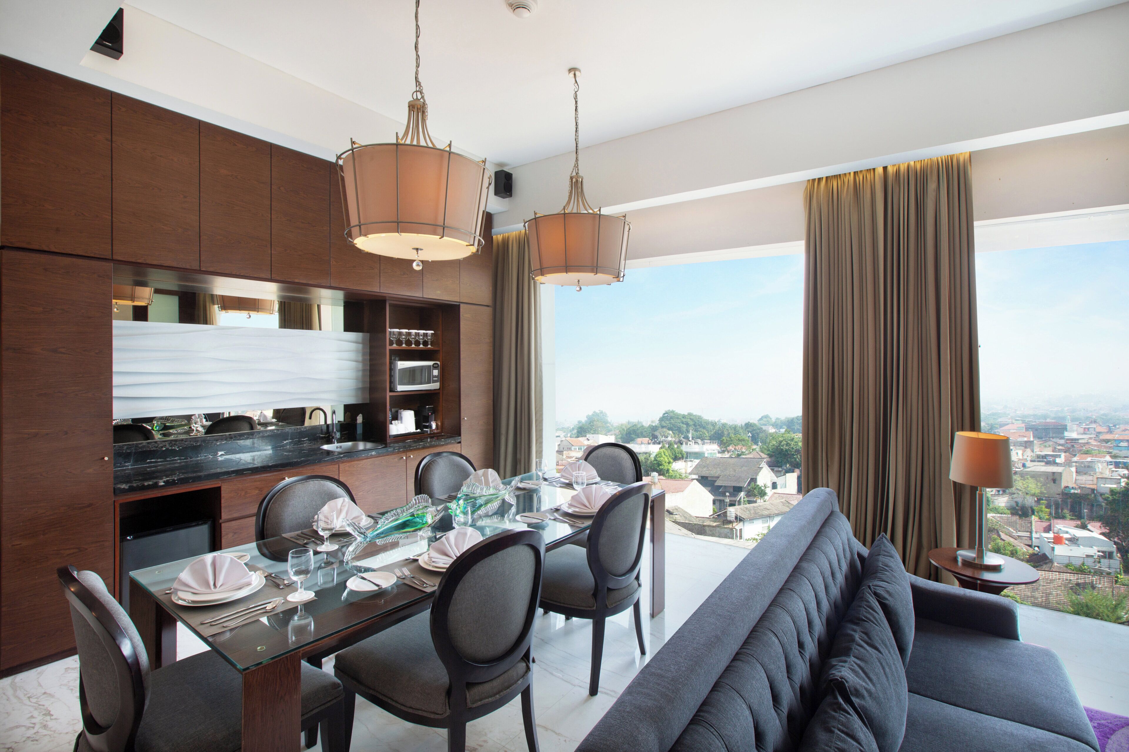 A modern dining area with a glass table, chairs, and a view of a cityscape through large windows.
