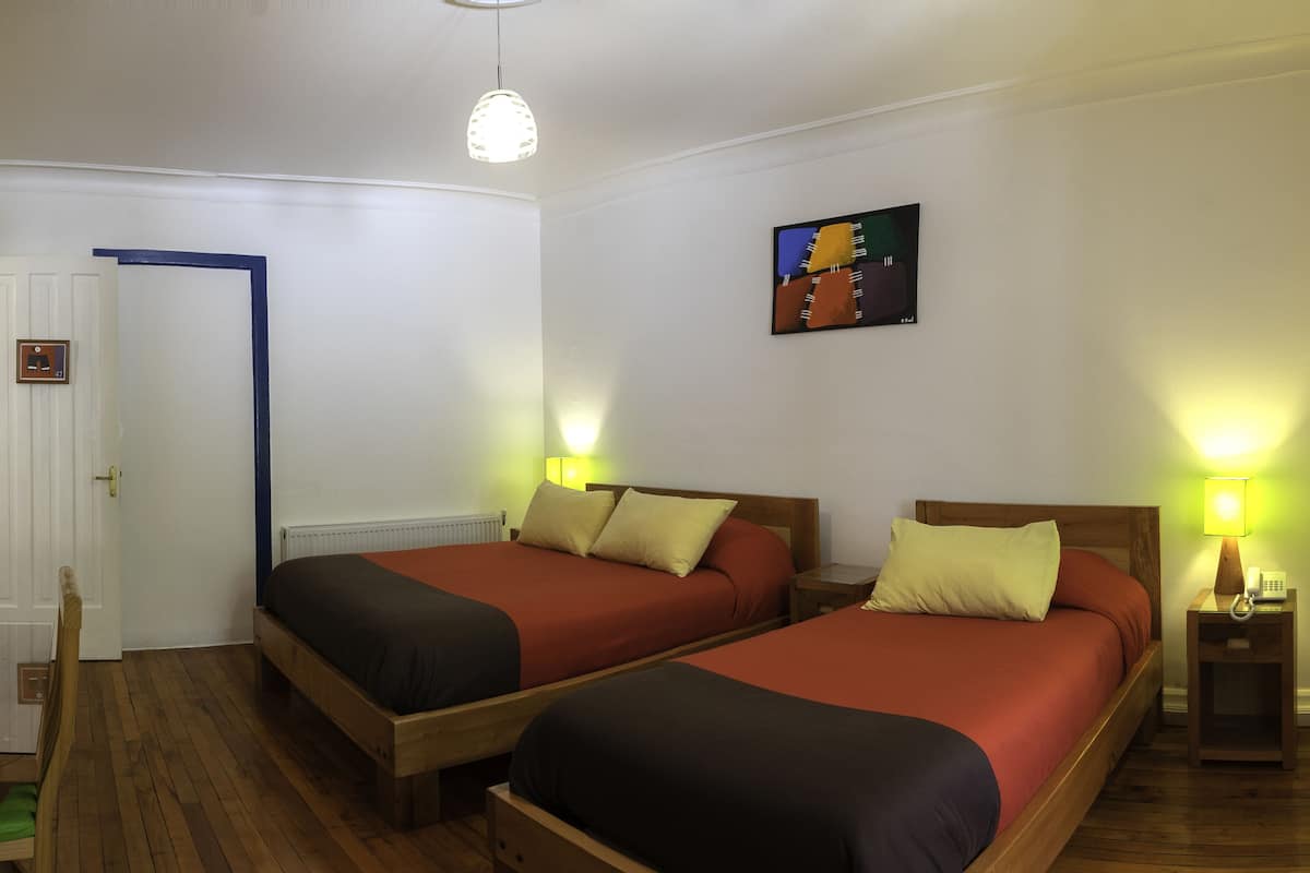 Habitación de hotel con dos camas, suelo de madera, una puerta con marco azul y un cuadro en la pared.