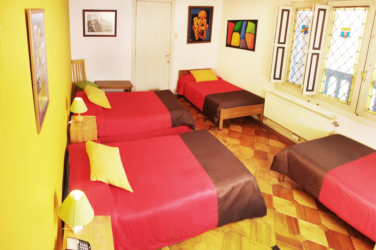 Habitación de hotel con cuatro camas, piso de madera, escritorio con lámpara, teléfono y obras de arte en las paredes.