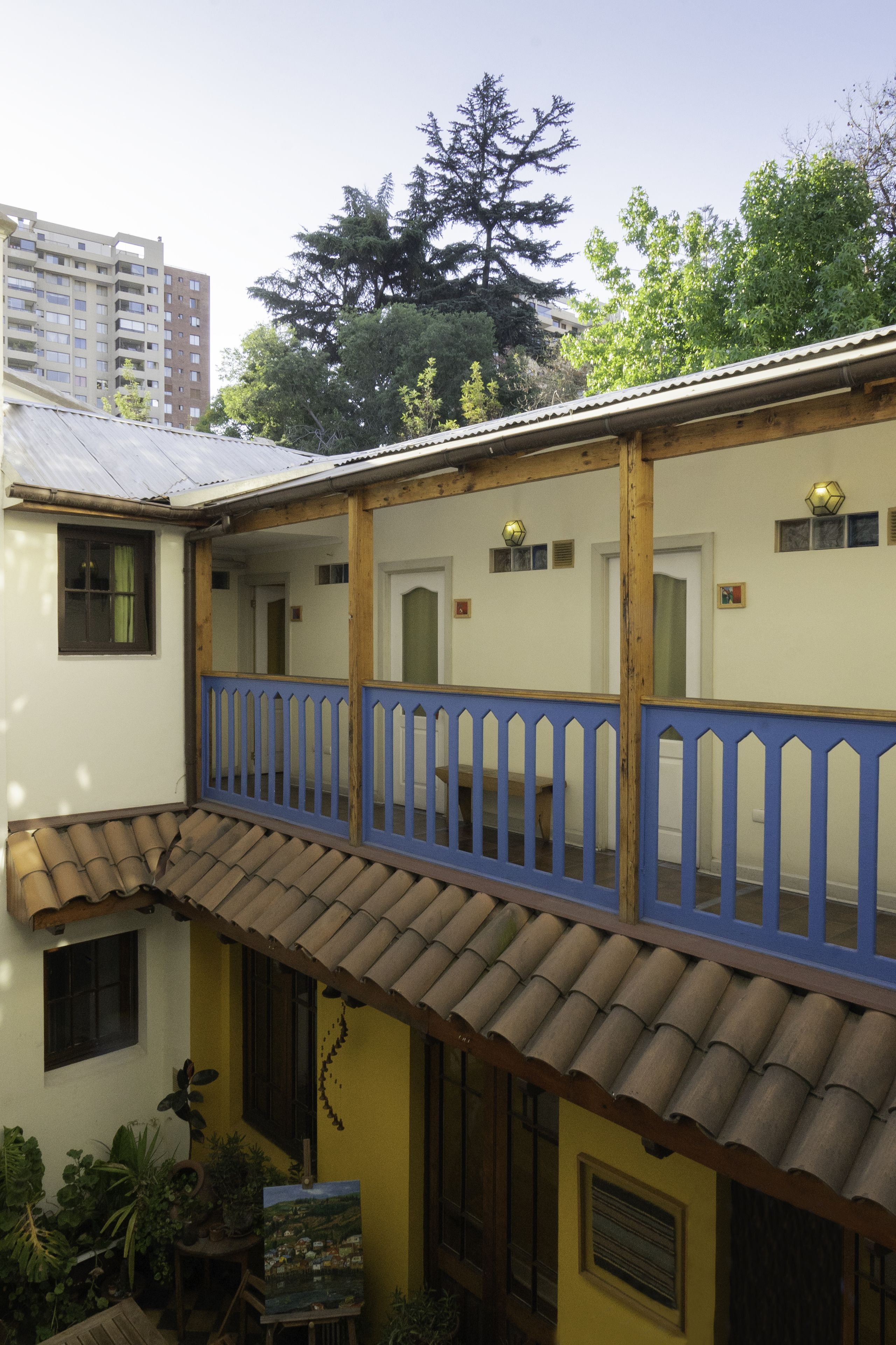 Un edificio de dos pisos con un balcón, un pequeño jardín y vistas a un árbol y un edificio al fondo.