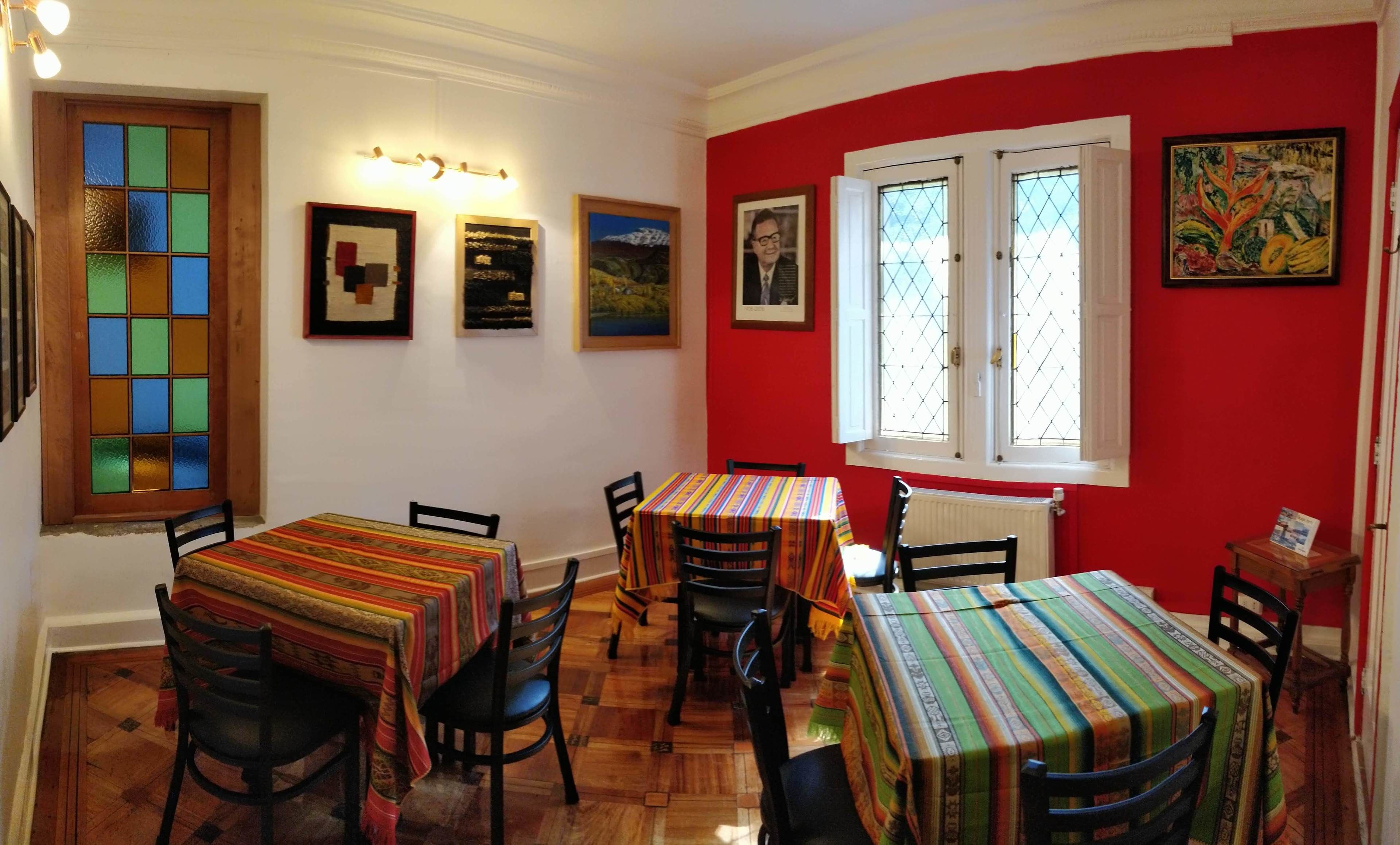 Un comedor con mesas cubiertas por manteles coloridos, sillas de madera y cuadros en las paredes.