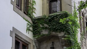 Ein Gebäude mit vielen Fenstern, einige mit Fensterläden, und einer Steinfassade, die mit Grün bewachsen ist.