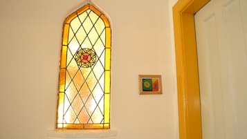 Une fenêtre en vitrail ornée de motifs géométriques, un chambranle de porte blanc et un petit tableau encadré accroché au mur.