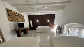 Ein Hotelzimmer mit einem Bett, einem Schreibtisch mit Computer, einem Fernseher und einem Deckenventilator.
