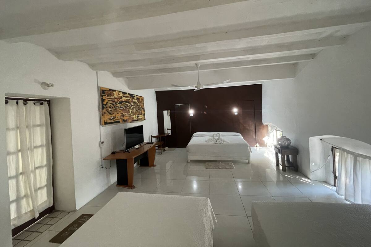 Una habitación de hotel espaciosa con una cama grande, un televisor de pantalla plana, un escritorio de madera y un ventilador de techo.