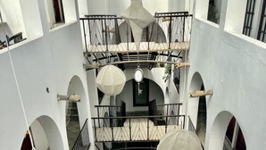 Ein mehrstöckiger Innenhof mit weißen Wänden, Rundbogentüren und hängenden Sonnenschirmen.