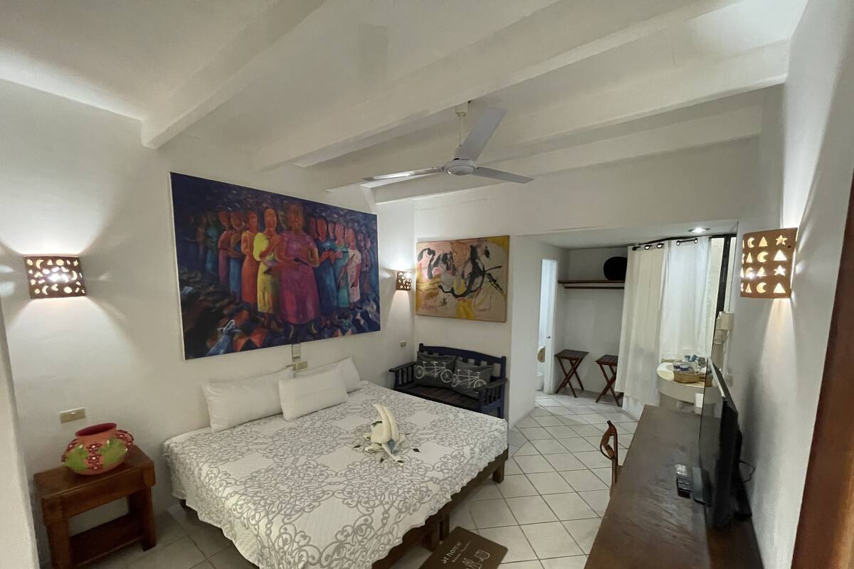Un dormitorio con cama, ventilador de techo y dos cuadros en la pared.