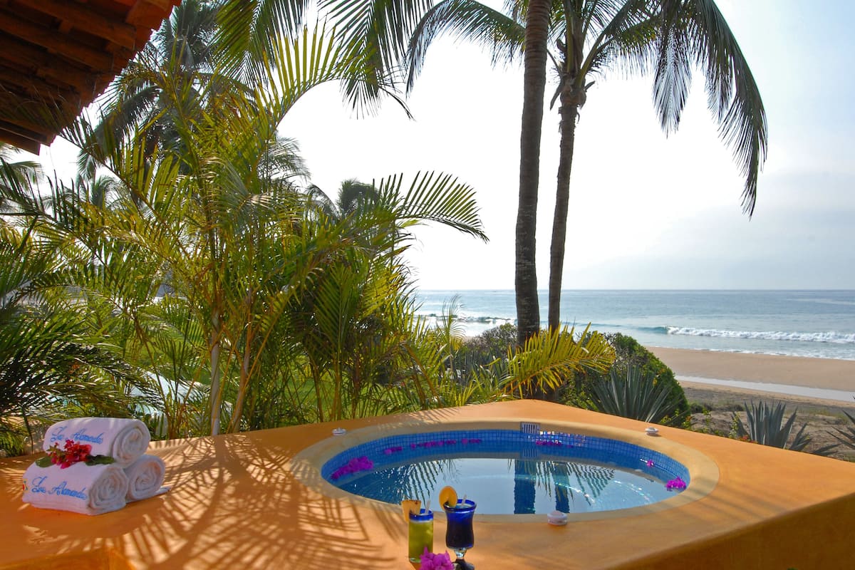 A pool area with a view of the beach and ocean, surrounded by palm trees.