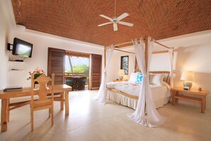 A bedroom with a four-poster bed, a ceiling fan, a TV, a wooden desk, and a chair.