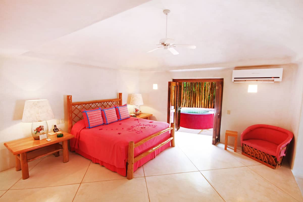 A bedroom with a bed, two bedside tables, a nightstand, a chair, a ceiling fan, and an air conditioning unit.