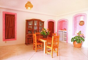 Un comedor con mesa y sillas de madera, un aparador con puertas de cristal y una planta en maceta.