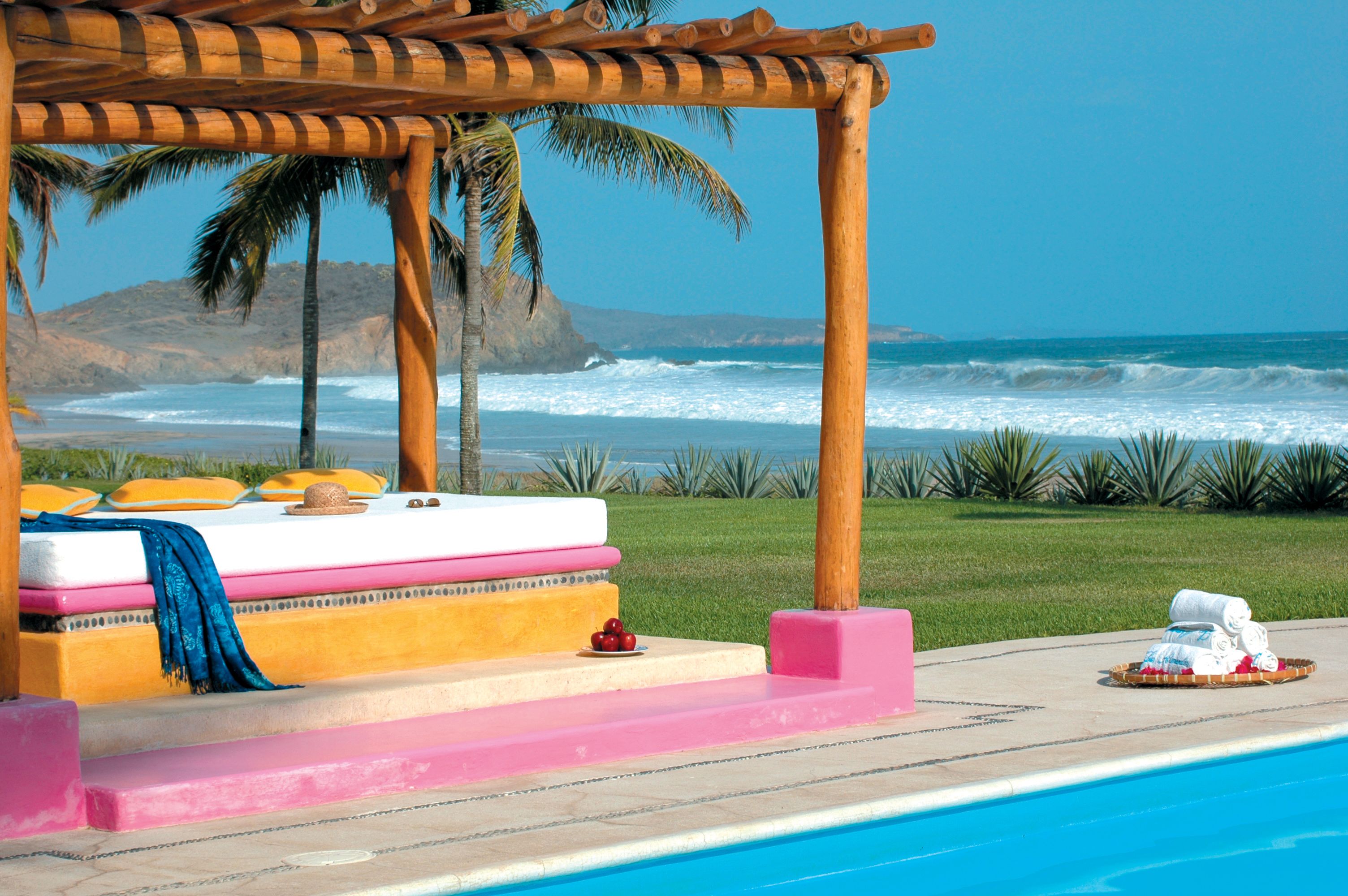 Uma área de piscina à beira-mar, com espreguiçadeira, toalhas e um cesto de objetos.