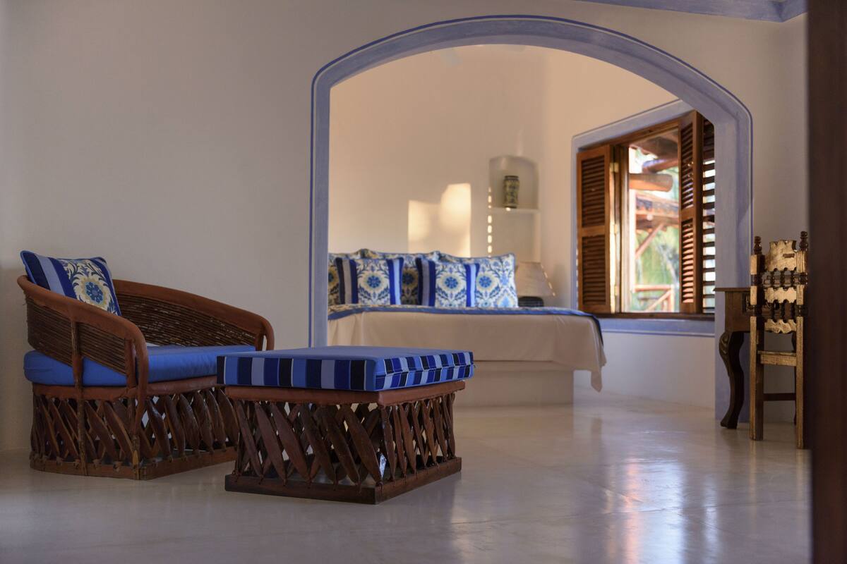 A room with wicker furniture, a bed with blue and white bedding, and a window with wooden shutters.