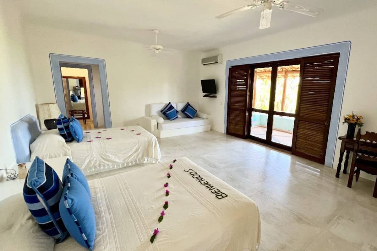A hotel room with two beds, a desk, a chair, a TV, and a large window with shutters.