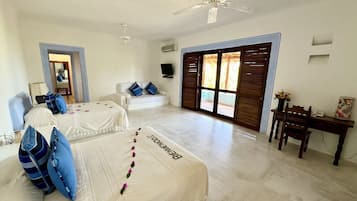 Habitación de hotel con dos camas, un escritorio, una silla, un televisor y un ventanal grande con contraventanas.