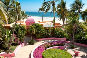 Un resort con un edificio de cúpula rosa, palmeras y vista a la playa.