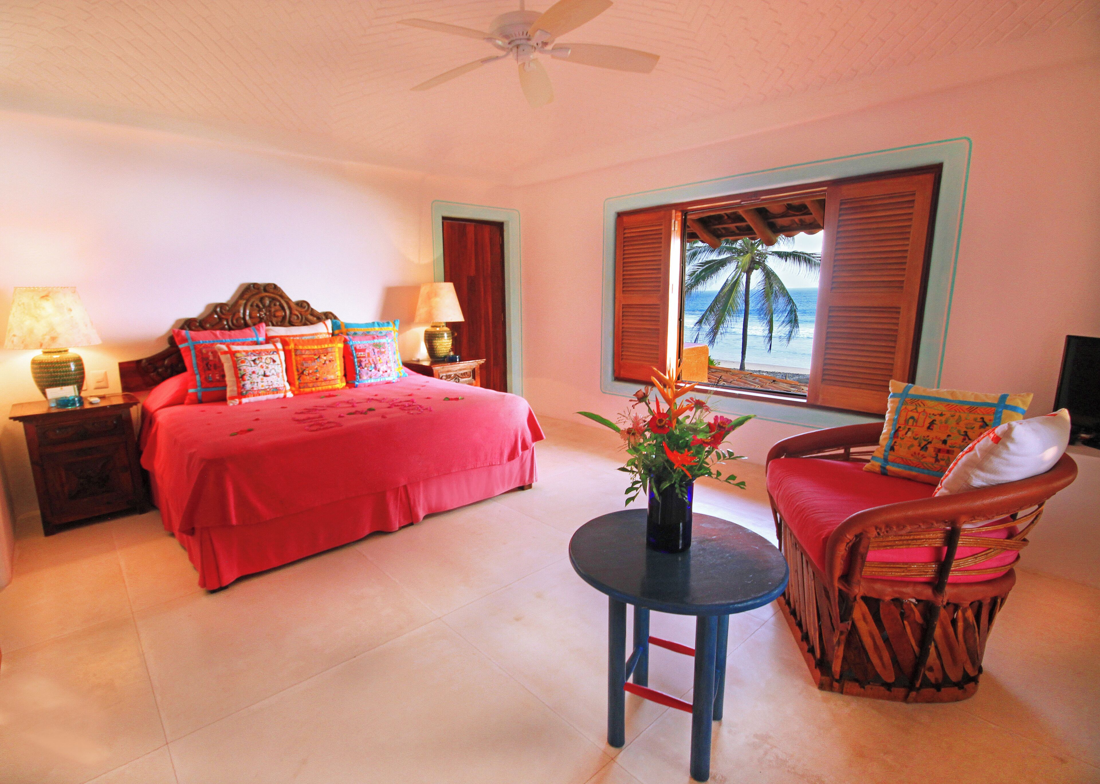 A bedroom with a bed, bedside tables, a chair, a table, and a window with shutters.