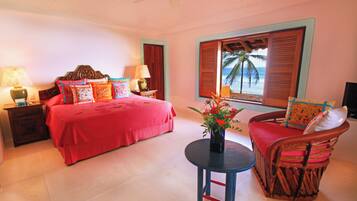 A bedroom with a bed, bedside tables, a chair, a table, and a window with shutters.