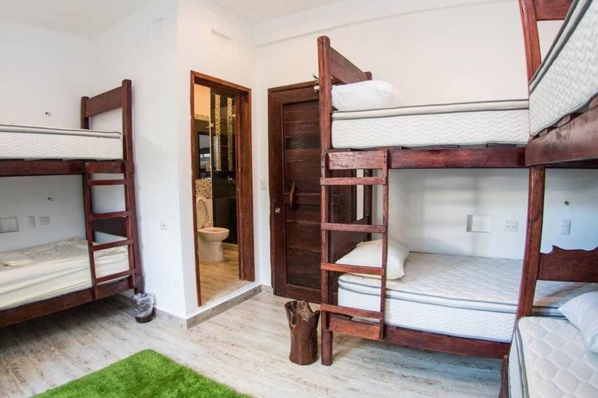 Ein Zimmer mit drei Etagenbetten, einer Holzleiter und einem kleinen Teppich.