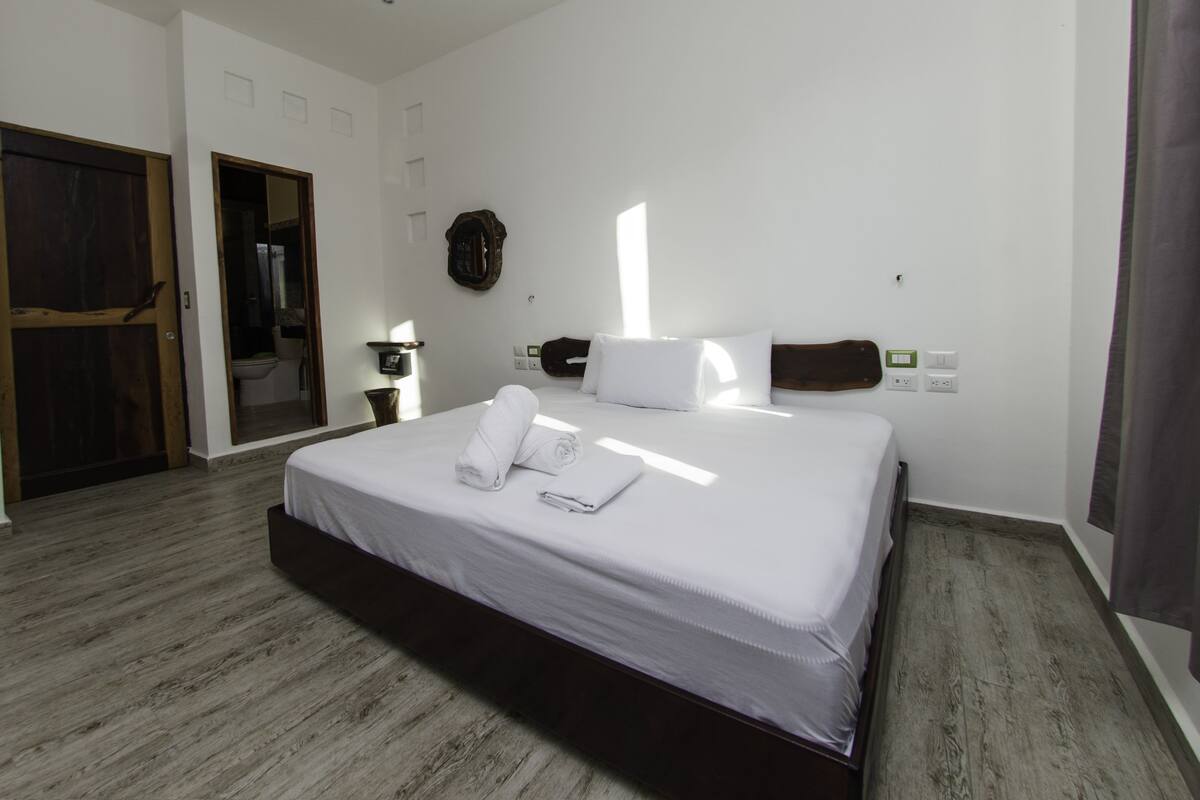 Ein modernes Hotelzimmer mit einem großen Bett, Holzboden, einem Spiegel und einem kleinen Nachttisch.