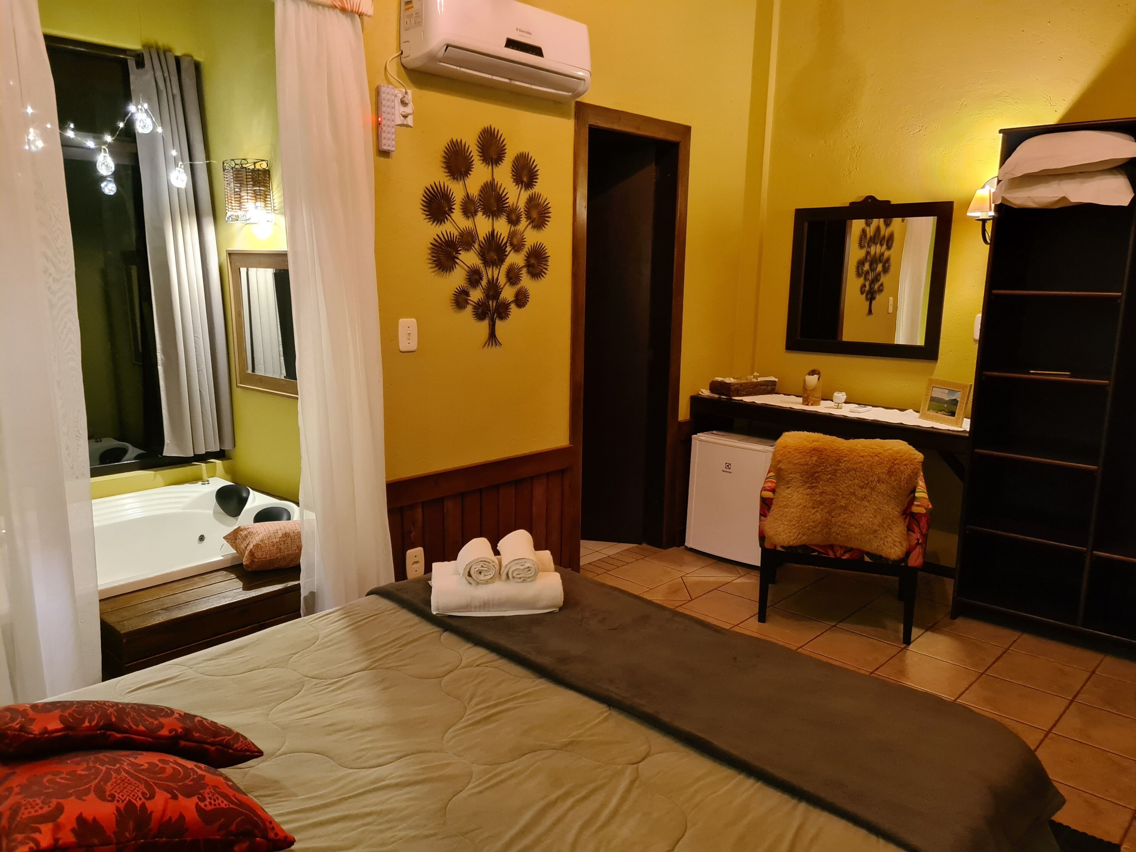 A hotel room with a bed, a desk, a chair, a small refrigerator, and a bathroom with a bathtub and shower.
