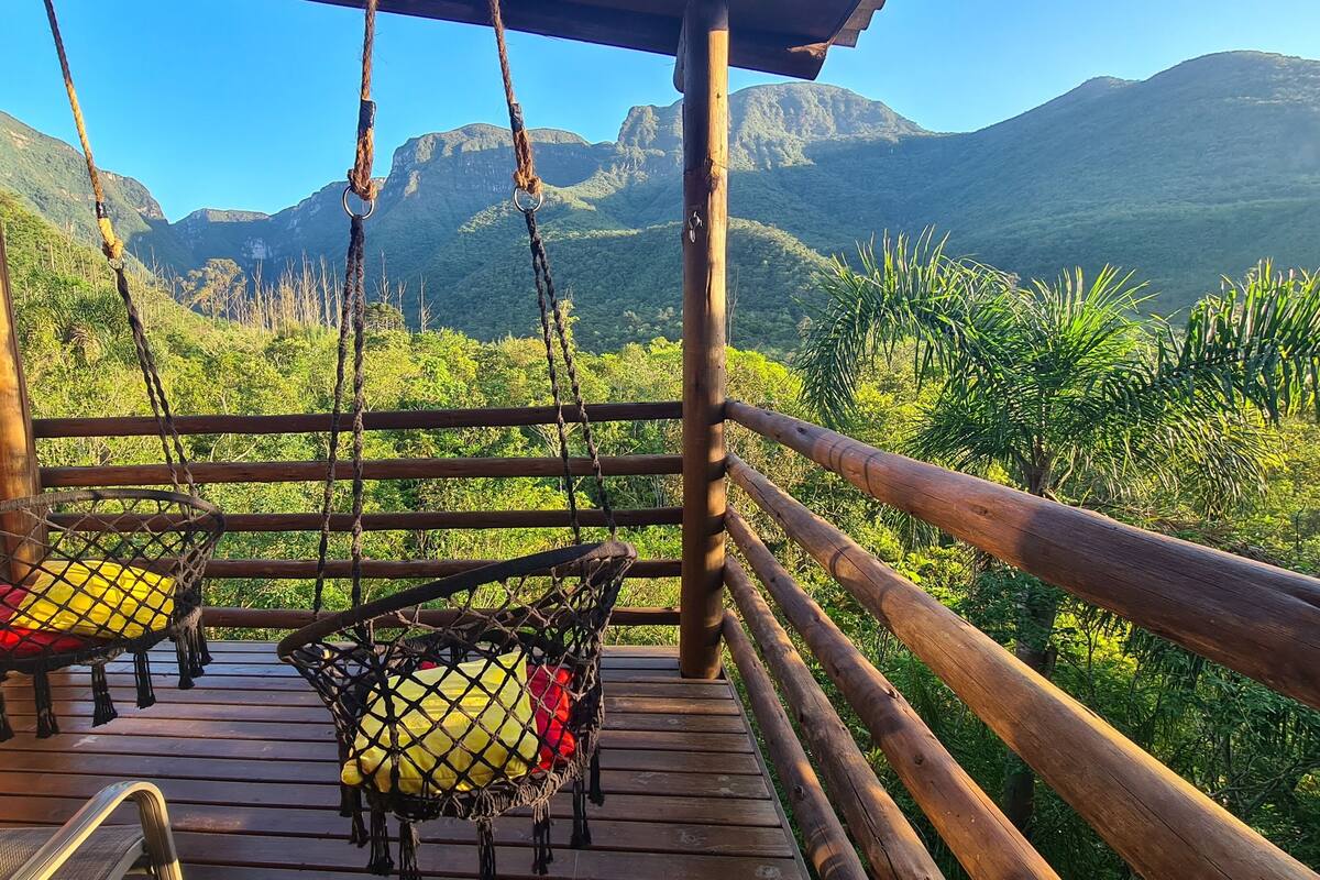 Terraza de madera con dos columpios y una silla, con vistas a un paisaje montañoso.