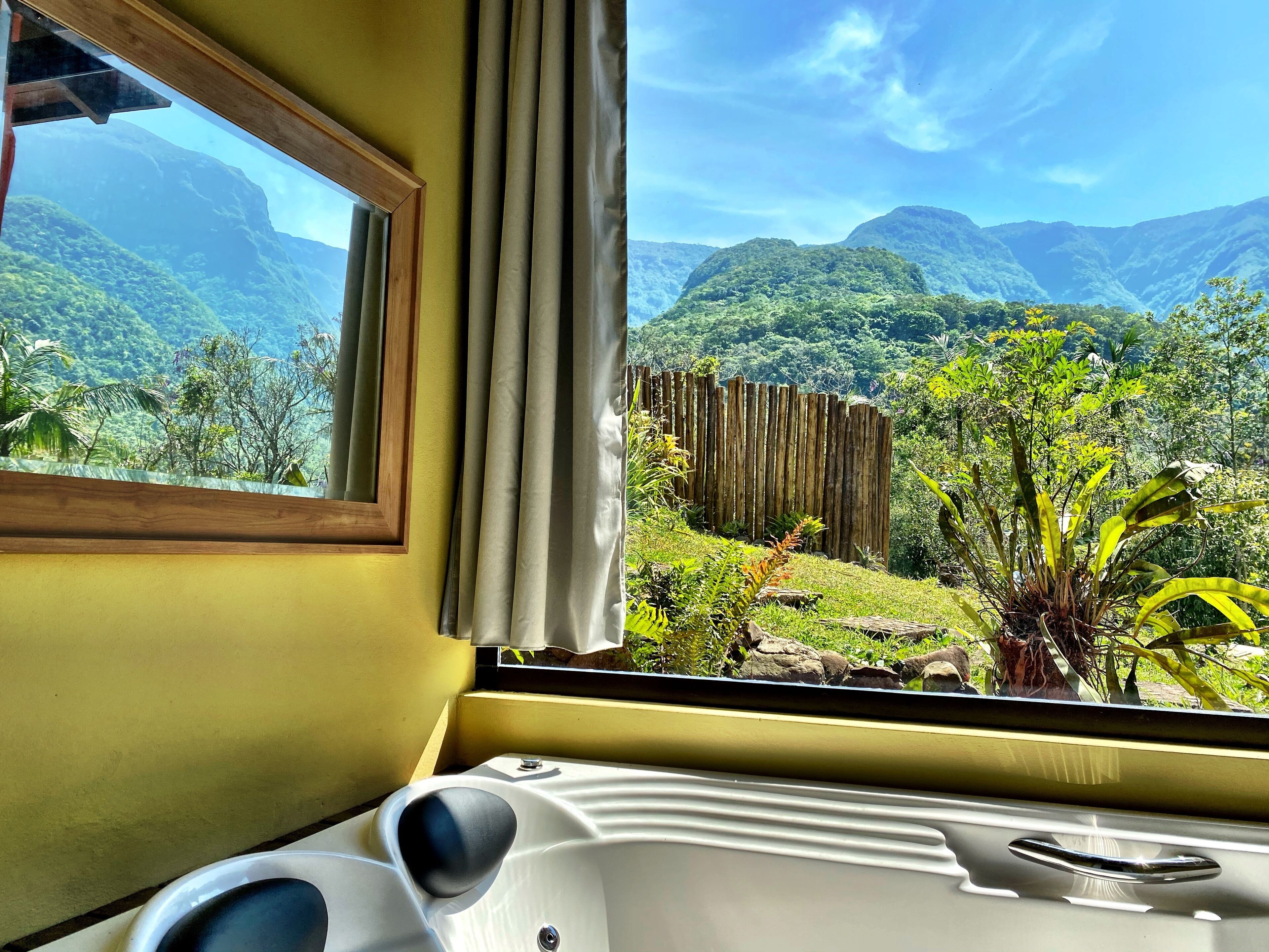 Quarto com vista para montanhas verdes exuberantes, cerca de madeira e janela com cortinas.