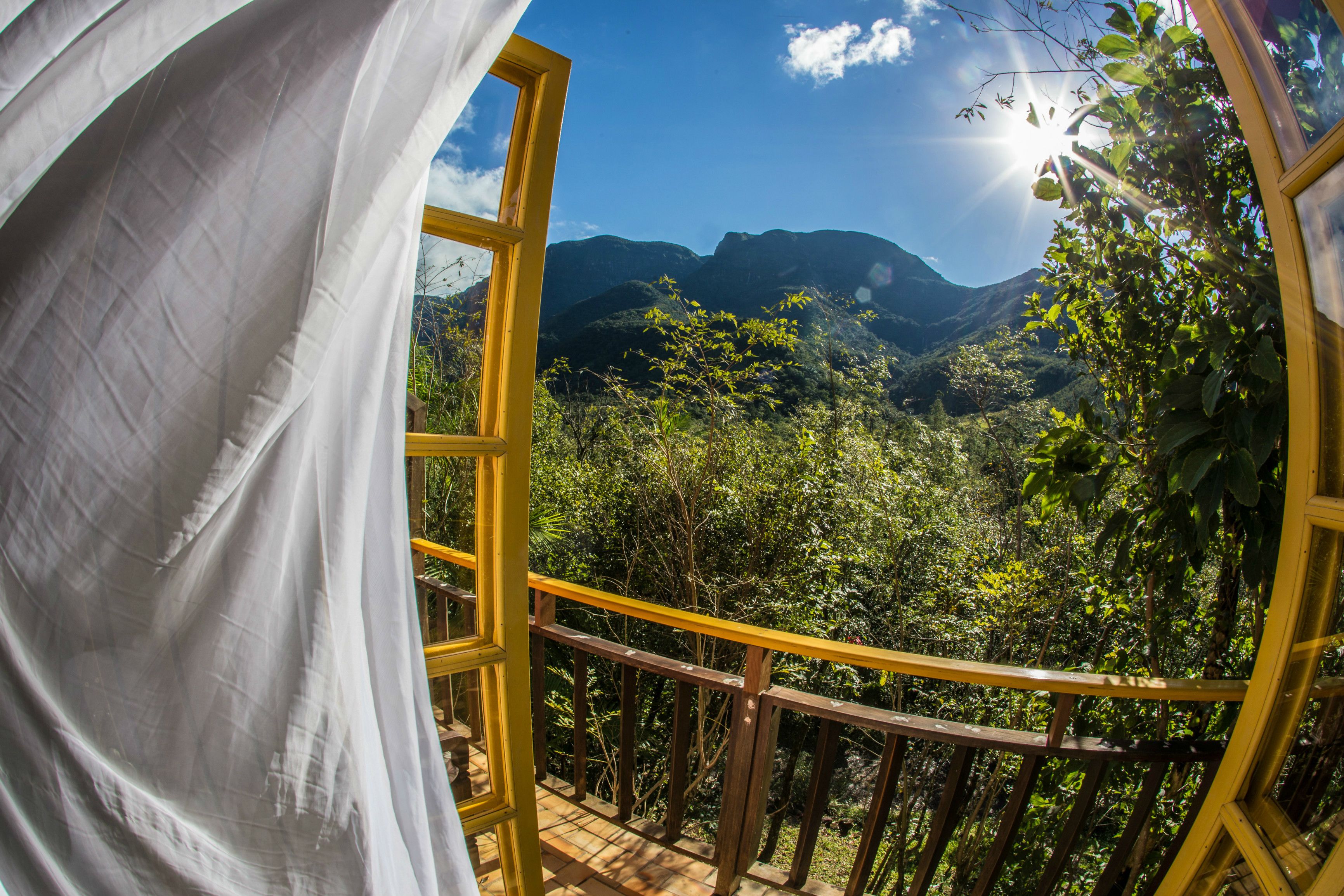 A balcony with a yellow railing overlooking a lush valley and mountains.