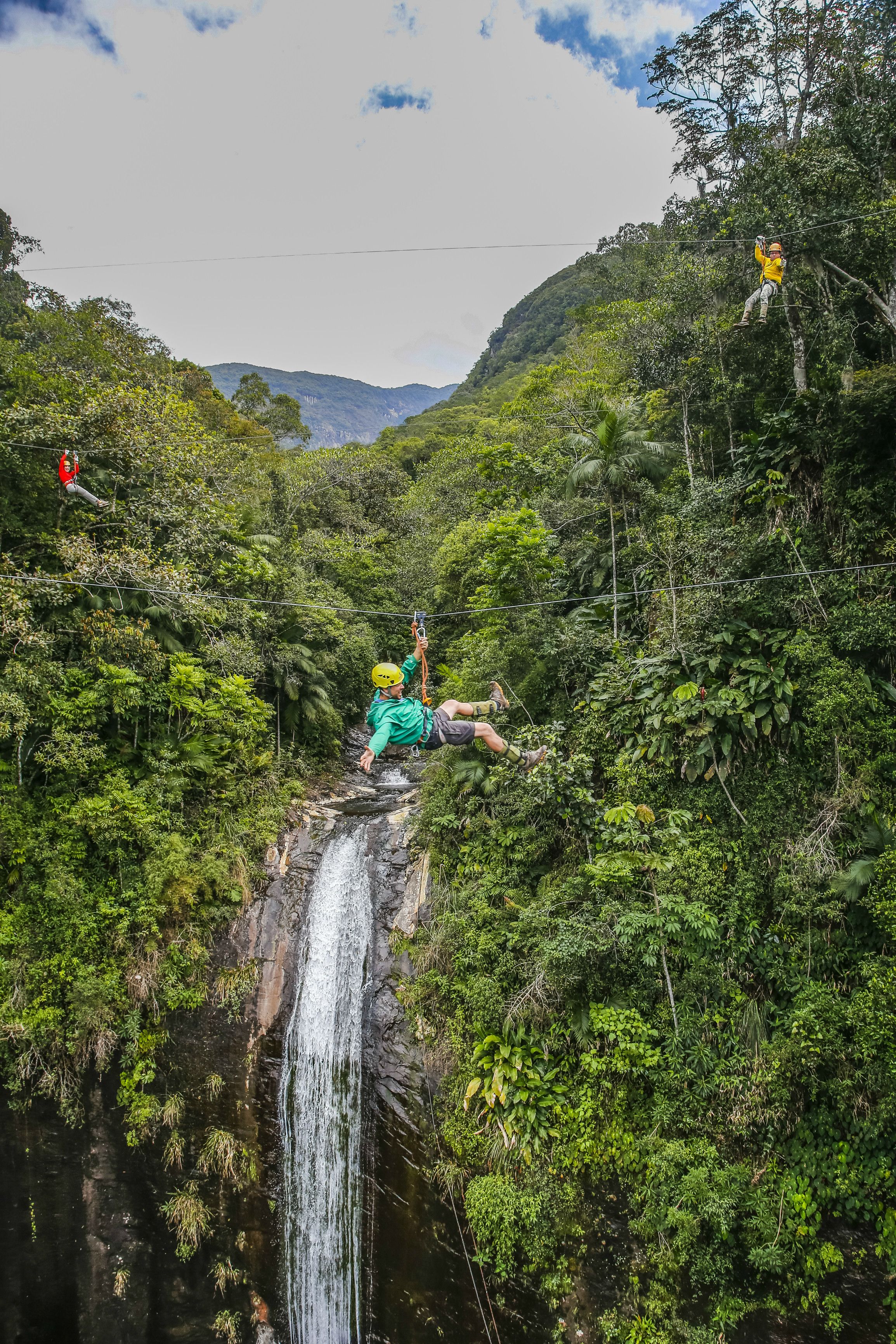 Iemand zoeft over een weelderig, groen bos, met een waterval op de achtergrond.