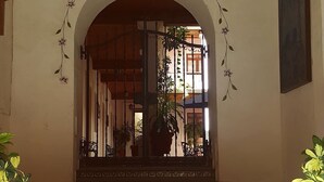 Ein überdachter Eingangsbereich mit einem dekorativen Bogen, einer Kandelaber und Blick auf ein Gebäude mit einem Balkon.