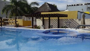 Una piscina con una estructura de sombrilla, un edificio de techo de paja y una palmera al fondo.