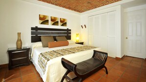 Un dormitorio con techo de ladrillo, una cama con colcha estampada, una mesita de noche con lámpara y una silla.