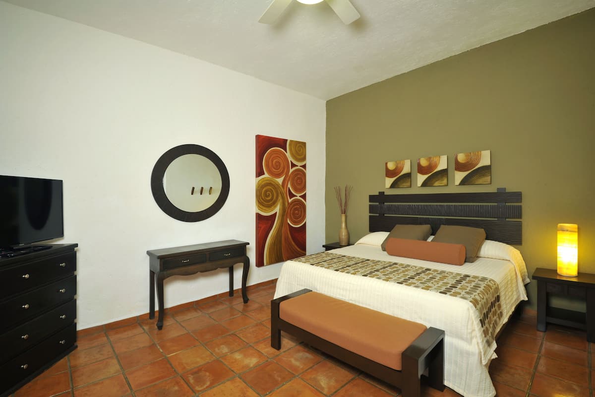 Een hotelkamer met een bed, een televisie, een nachtkastje, een bankje en kunst aan de muren.