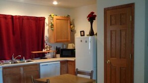 Una cocina compacta con armarios de madera, microondas, refrigerador, lavamanos y una mesa de comedor con sillas.