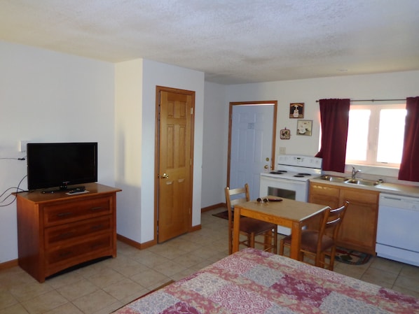 A compact kitchen with a stove, sink, and a dining area with a table and chairs. - El Vu Motel (Bowman)