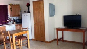 Una cocina compacta con una mesa y sillas, un refrigerador, una puerta de madera y un televisor sobre un mueble.
