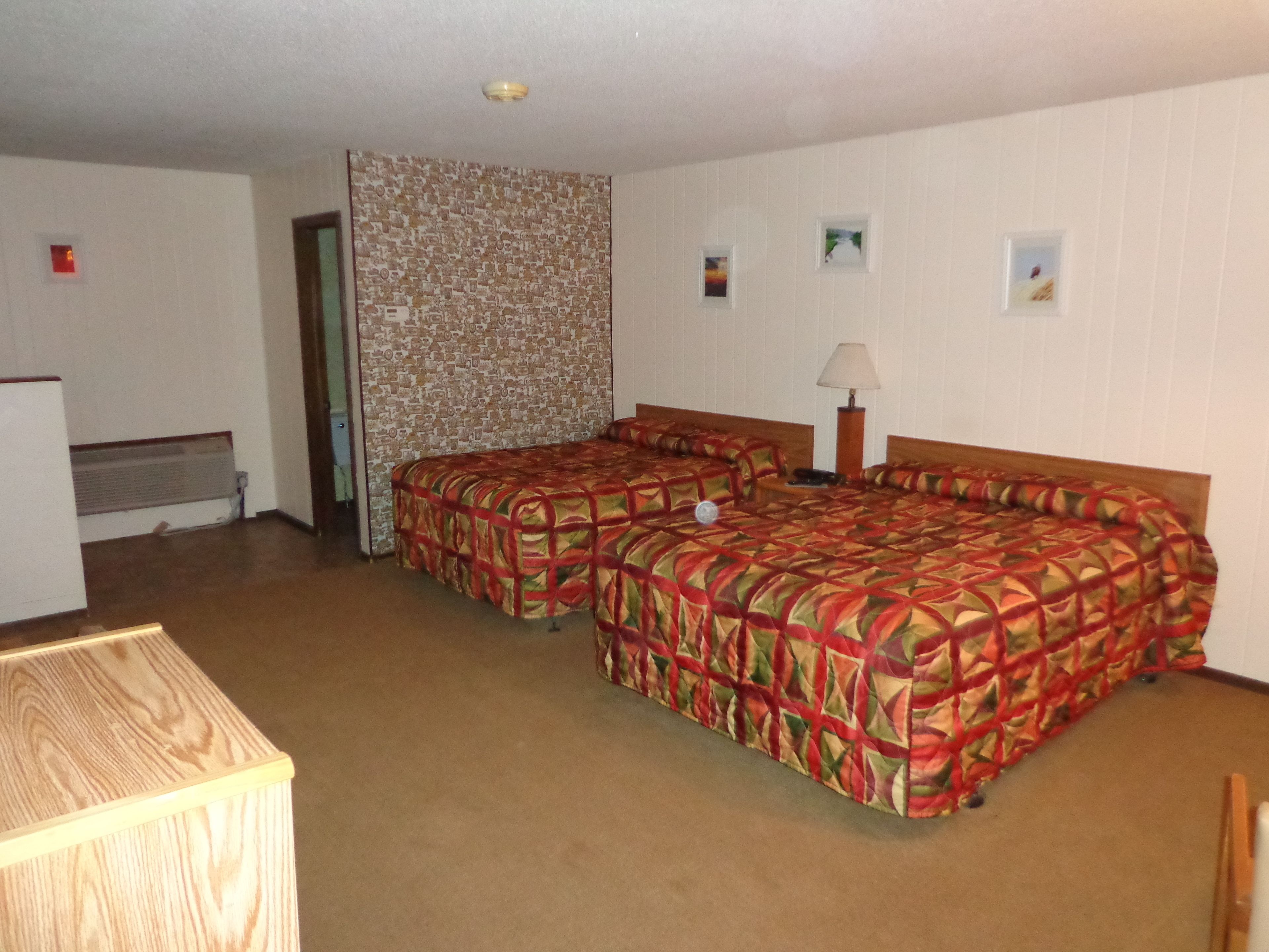 A hotel room with two beds, a wooden desk, a lamp, and a patterned wall.