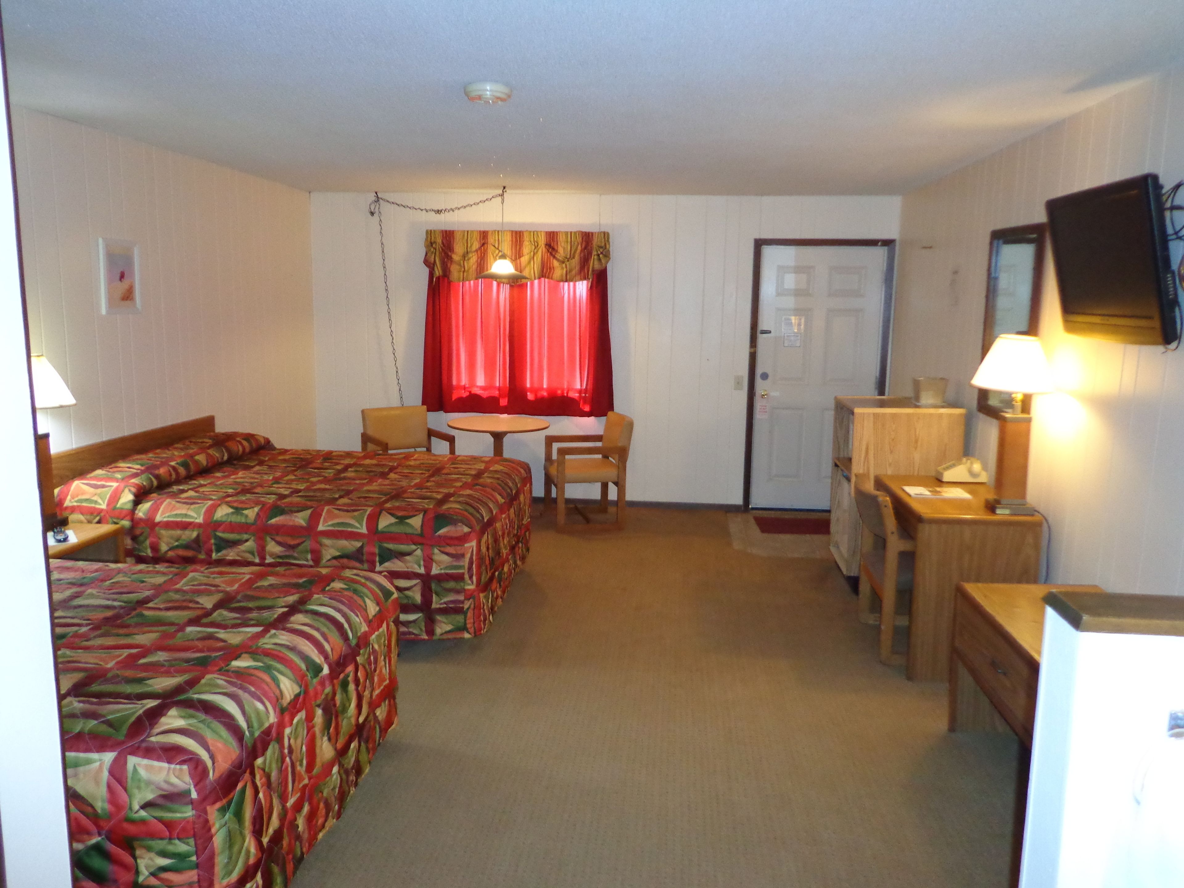 A hotel room with two beds, a desk, a chair, a table, and a television.